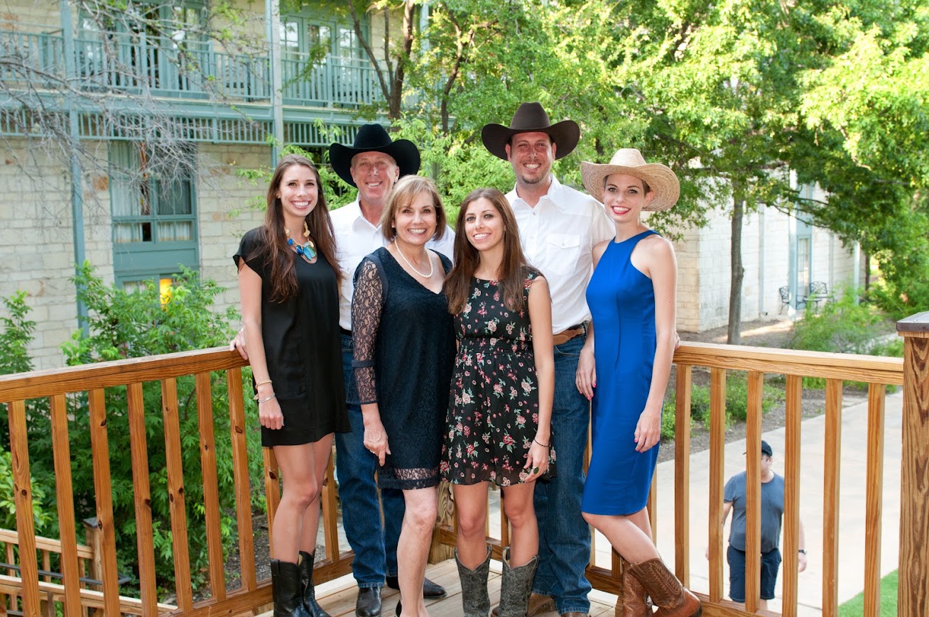 A family dressed in cowboy hats and boots gathered on a wooden deck in the Texas Hill Country